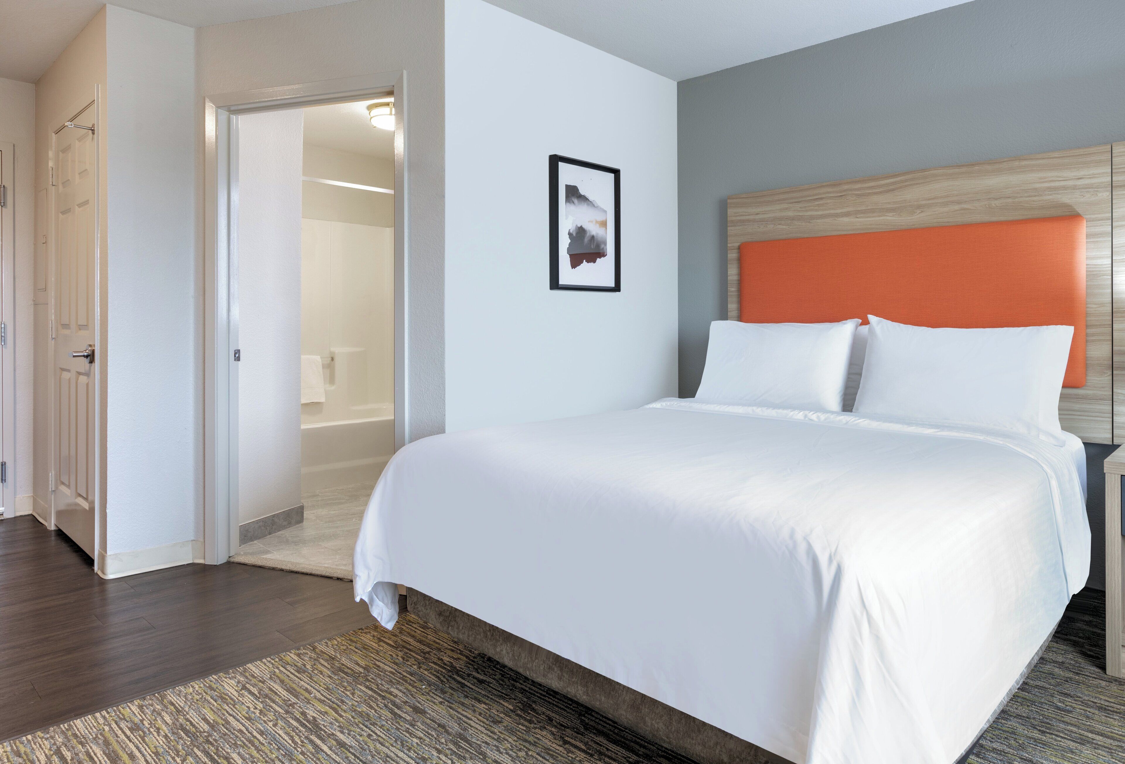 A hotel room with a large bed, a wooden headboard, a framed picture on the wall, and a walk-in closet.