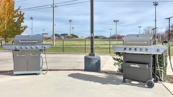 Twee buitenbarbecues, een betonnen pad en een honkbalveld op de achtergrond.