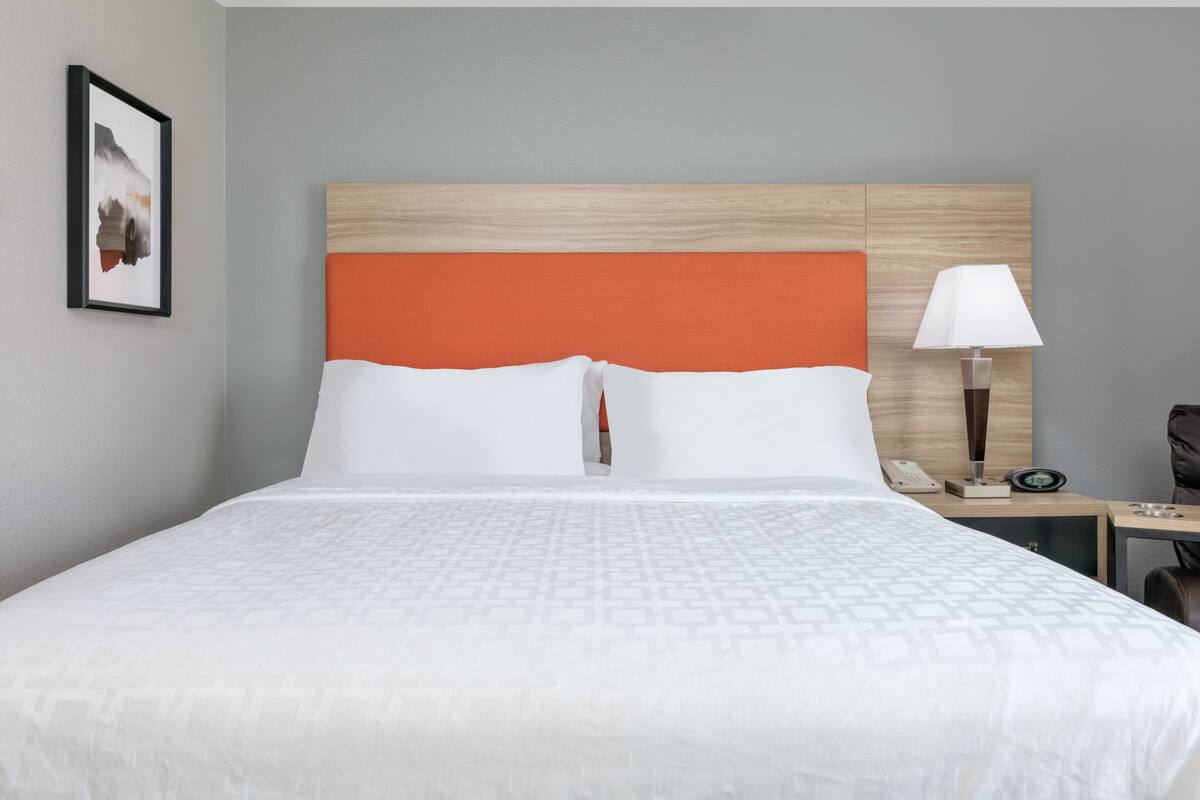 Een hotelkamer met een bed, nachtkastje, lamp en een ingelijst schilderij aan de muur.