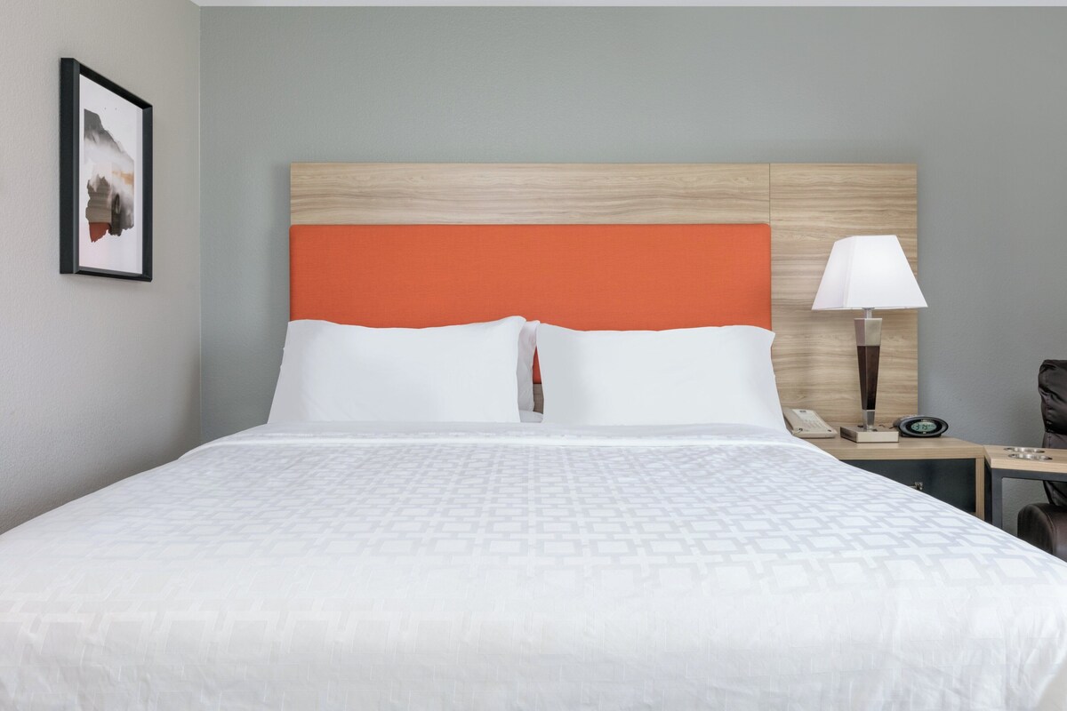 Een hotelkamer met een bed, nachtkastje, lamp en een ingelijst schilderij aan de muur.
