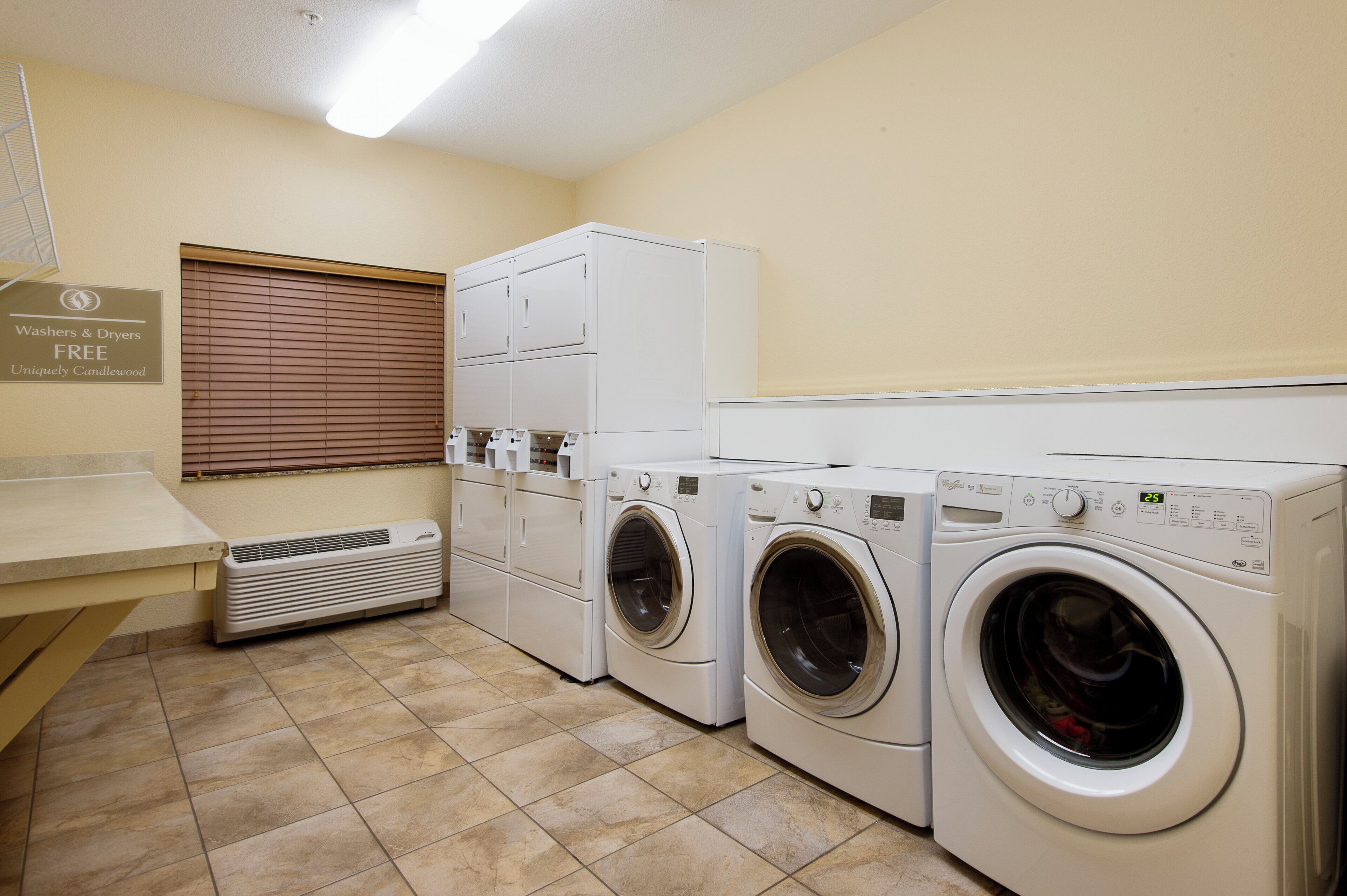 A laundry room with a sign indicating free washers and dryers, a ventilation unit, and a tiled floor.