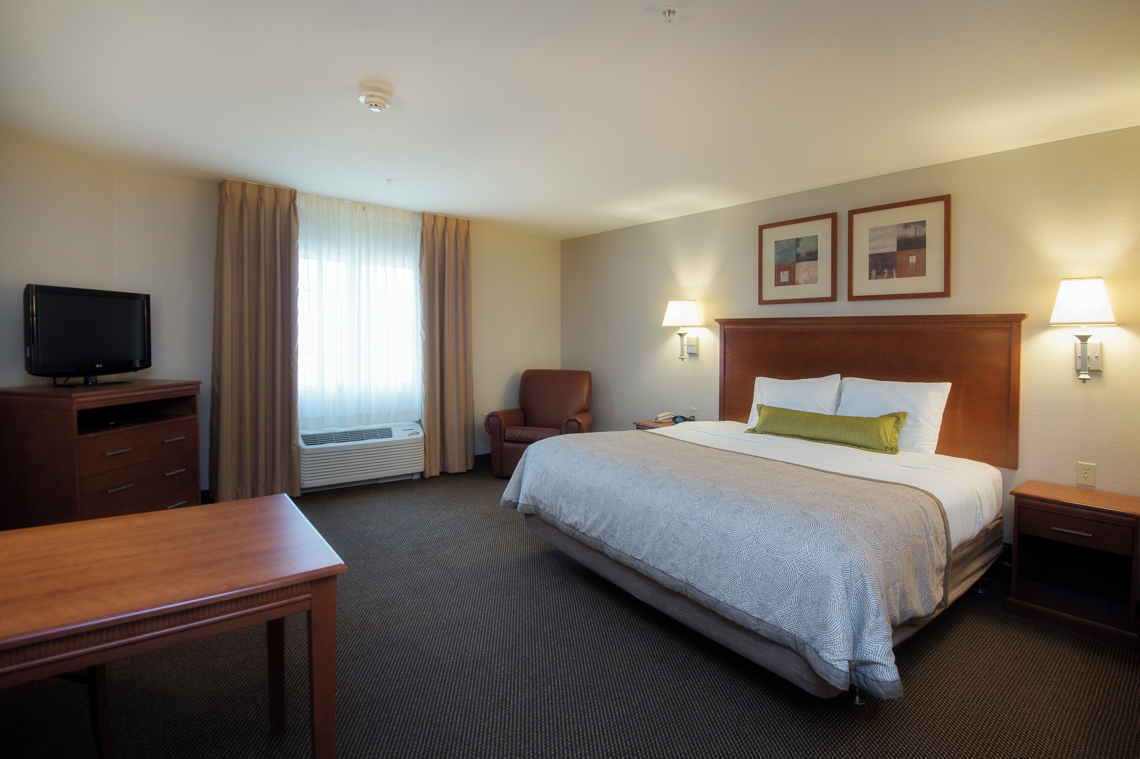 Ein Hotelzimmer mit Bett, Schreibtisch, Stuhl, Fernseher und zwei Wandlampen.