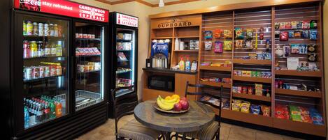 A snack bar with a refrigerator stocked with beverages, a microwave, and shelves with snacks and chips.