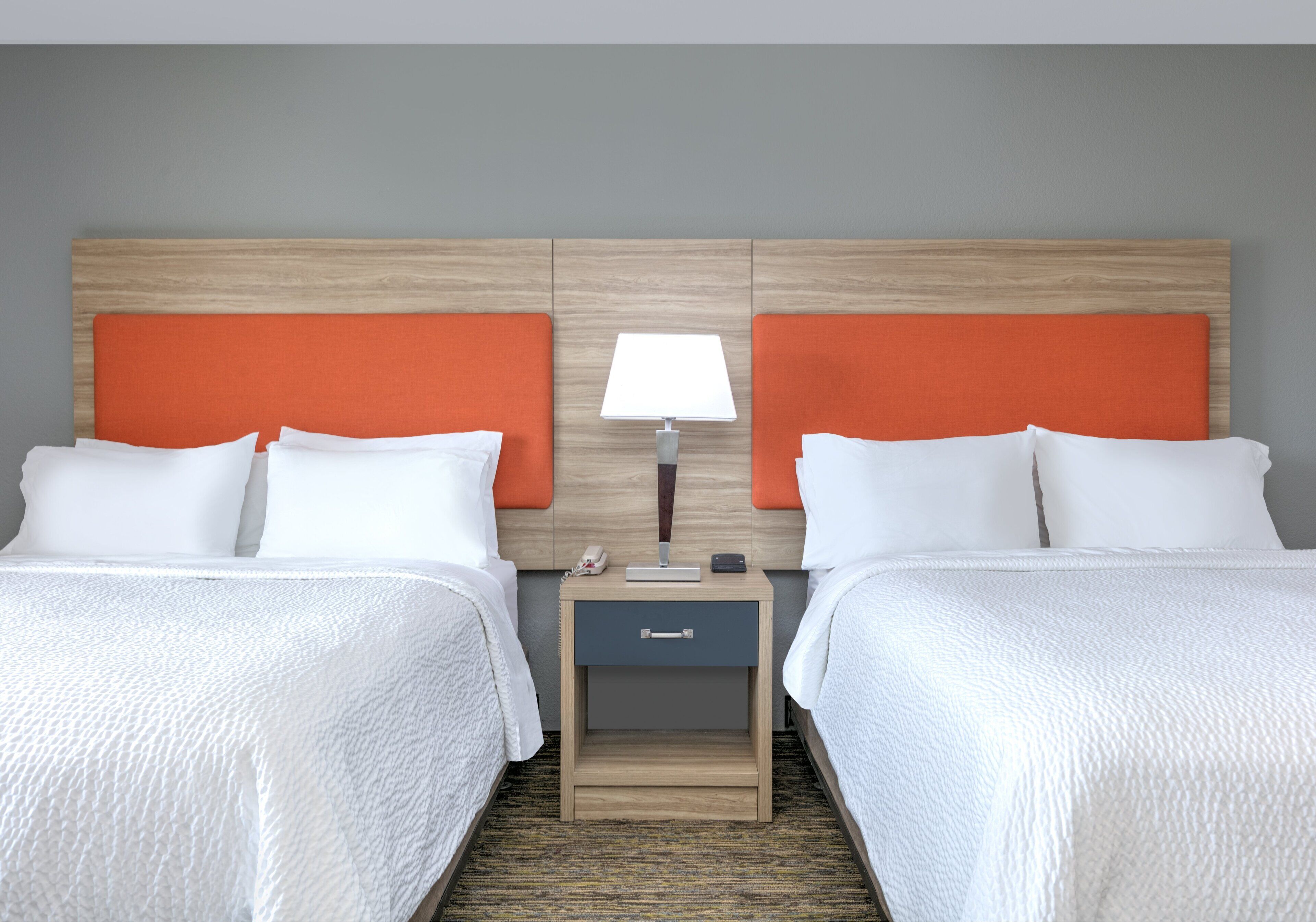 Ein Hotelzimmer mit zwei Betten, einem Nachttisch mit Lampe und einer kleinen Schublade.