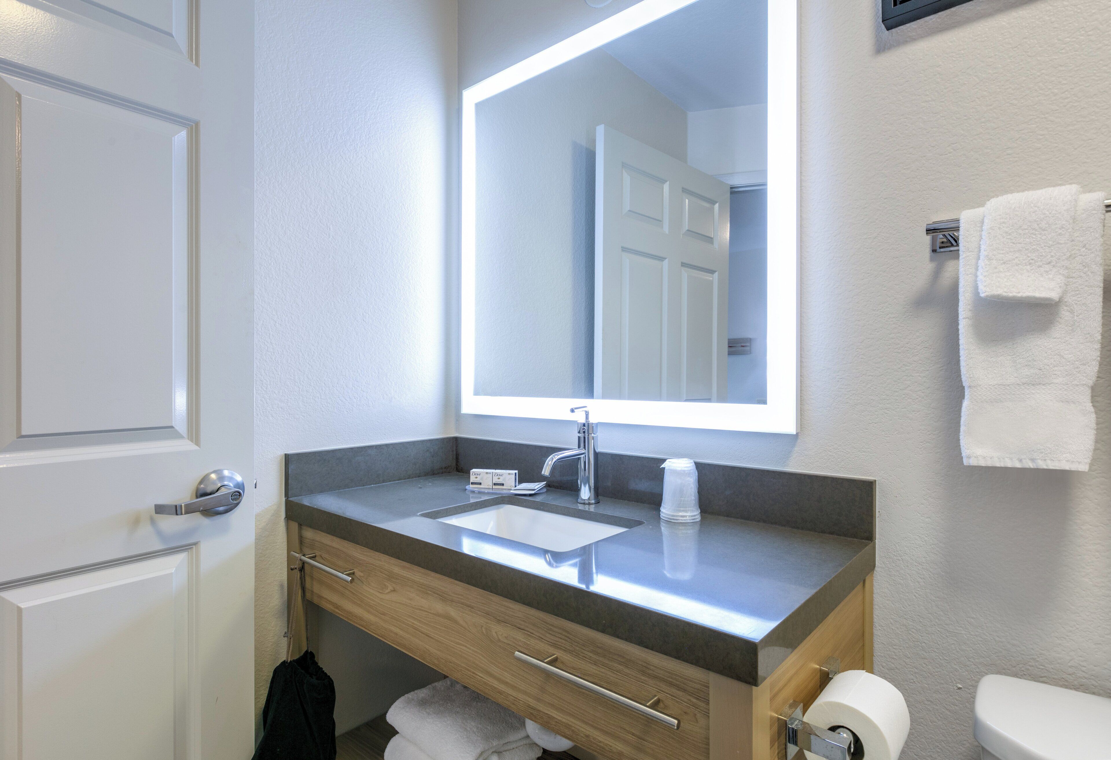 A modern bathroom with a large mirror, a sink, a toilet, and a towel rack.
