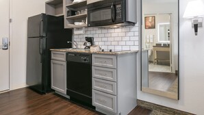Een moderne keuken met grijze kastjes, een zwarte koelkast, een magnetron en een koffiezetapparaat.