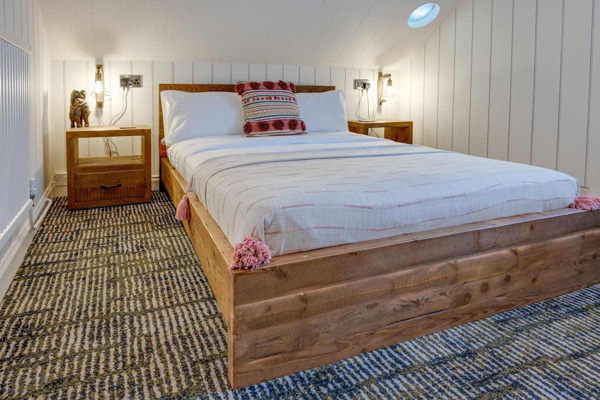 A wooden bed with white bedding, two bedside tables with lamps, and a patterned carpet.