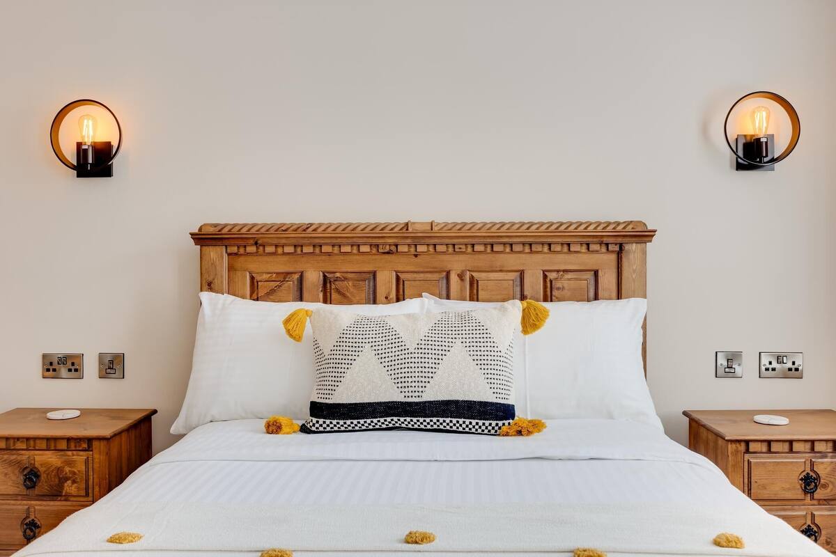 A neatly made bed with a wooden headboard, two bedside lamps, and a bedside table with a power outlet.
