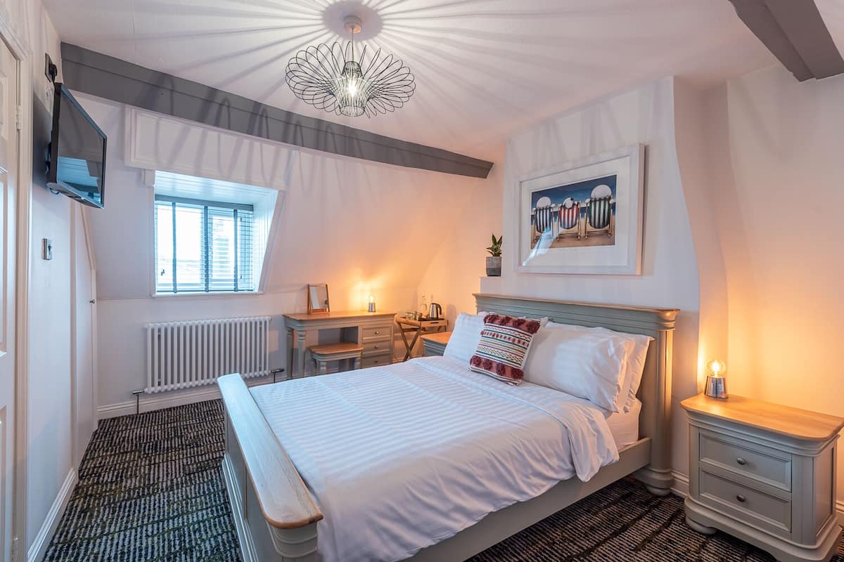 A bedroom with a bed, bedside tables, a dresser, a radiator, a window, and a ceiling light fixture.