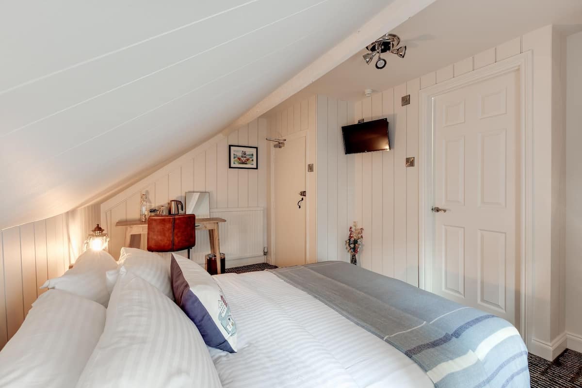 A bedroom with a bed, a bedside table, a lamp, a TV, and a door.