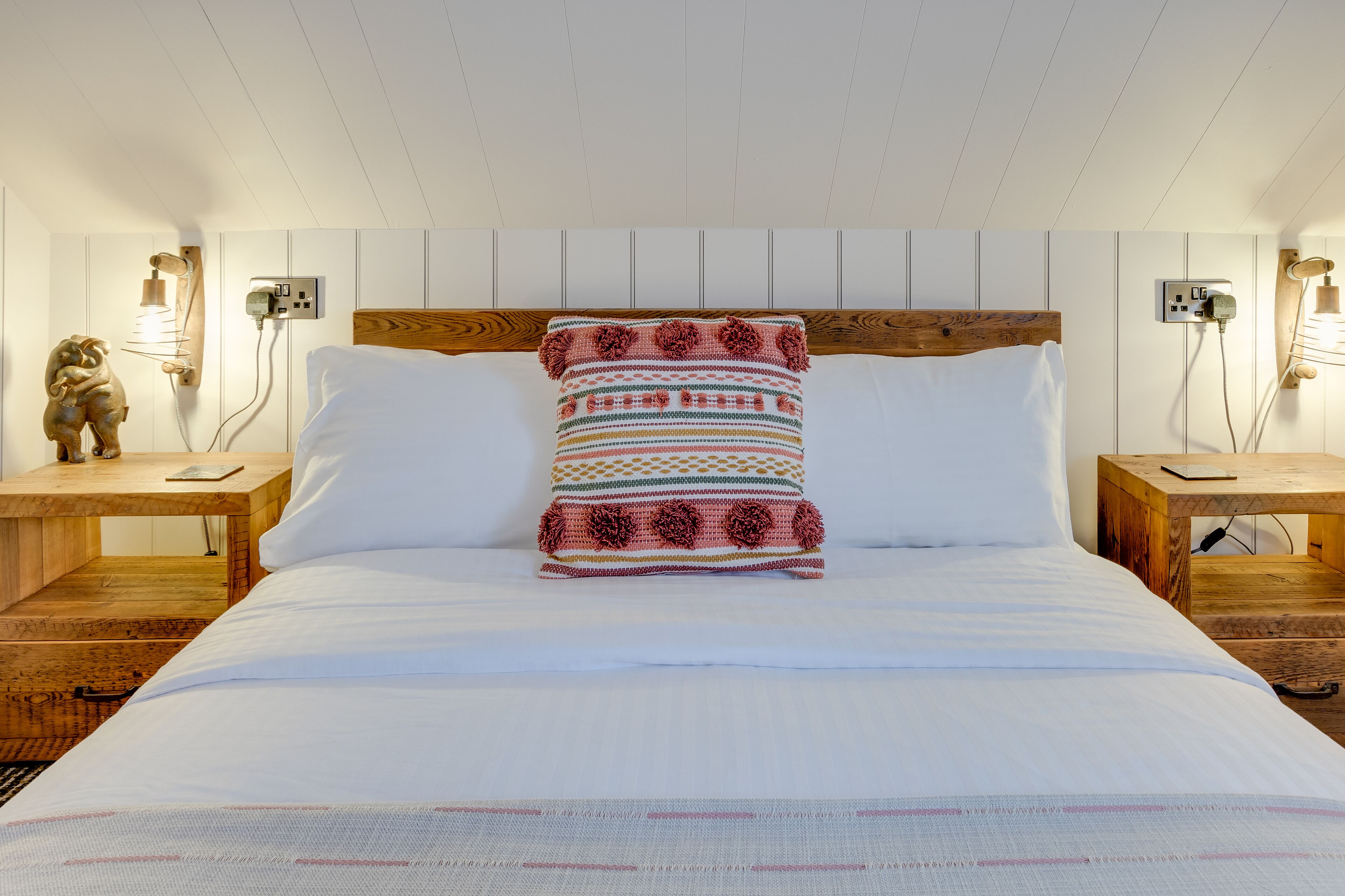 A neatly made bed with a patterned pillow, wooden headboard, and two bedside tables with lamps.