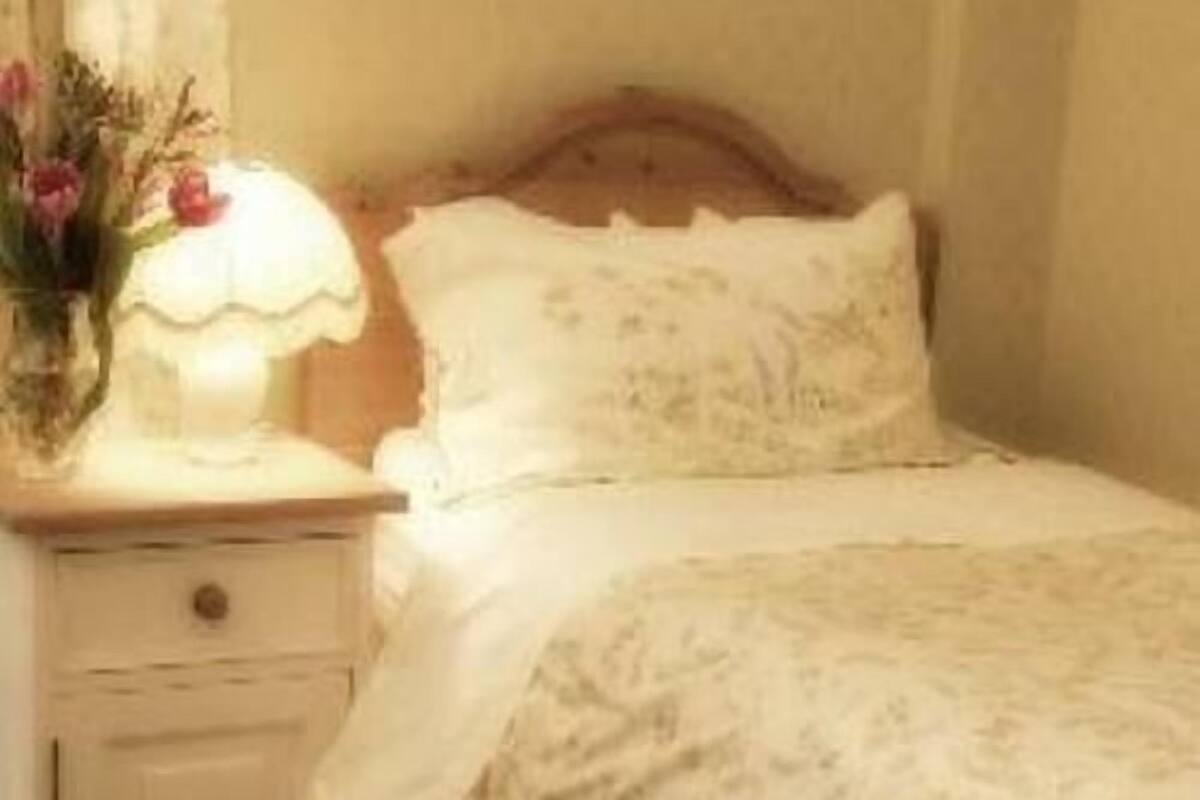 A bedroom with a wooden headboard, a bedside table with a lamp, and a floral arrangement.