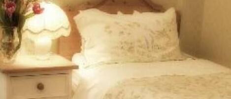 A bedroom with a wooden headboard, a bedside table with a lamp, and a floral arrangement.