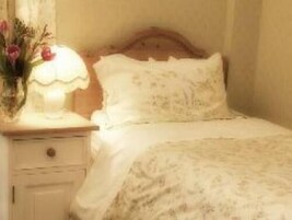 A bedroom with a wooden headboard, a bedside table with a lamp, and a floral arrangement.