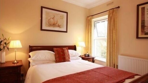 A neatly made bed with a red blanket, a bedside lamp, and a framed picture on the wall. - Murray House (Harrogate)