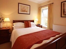 A neatly made bed with a red blanket, a bedside lamp, and a framed picture on the wall.