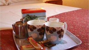 A tray with a box of tea, two floral mugs, a teapot, and a packet of tea bags on a bed. - Murray House (Harrogate)