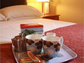 A tray with a box of tea, two floral mugs, a teapot, and a packet of tea bags on a bed.