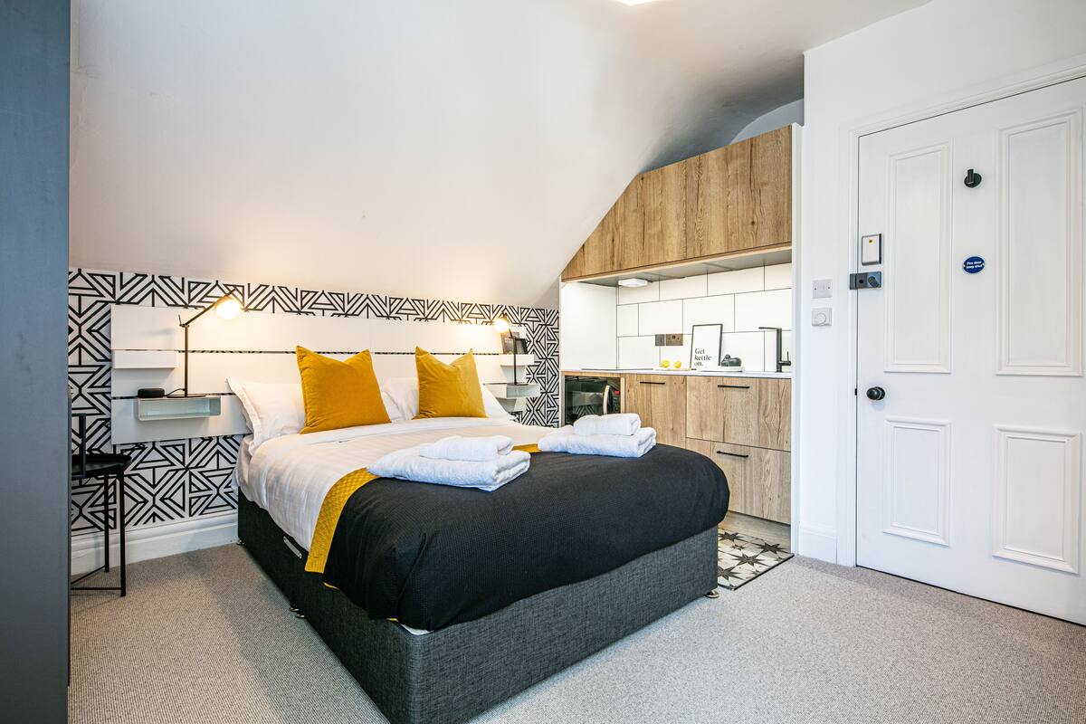 Ein modernes Schlafzimmer mit Bett, Nachttisch und Blick zur Küche.