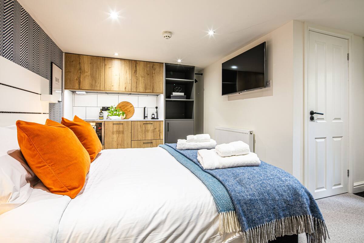 Ein modernes Schlafzimmer mit Bett, orangefarbenen Kissen, einer blauen Decke und einer weißen Tür.