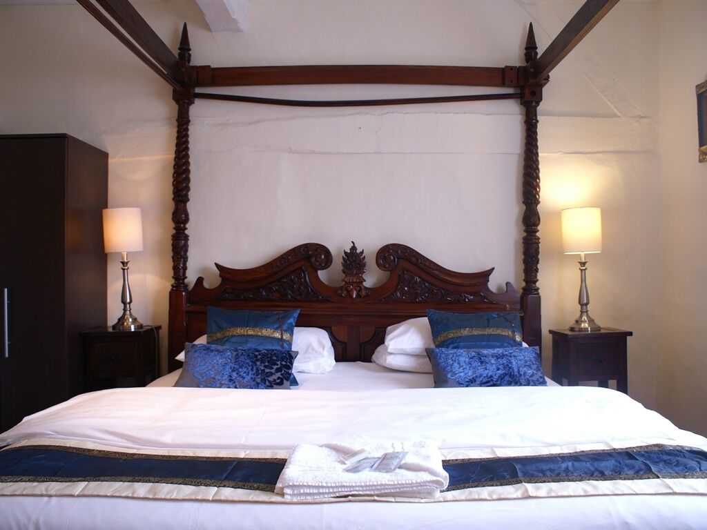 Una cama con dosel con cubrecama blanco y almohadas azules, flanqueada por dos mesitas de noche con lámparas.