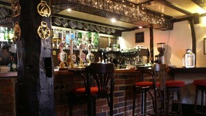 A bar area with stools, a brick wall, and a variety of bottles and glasses on the shelves. - The Saracens Head (Amersham)