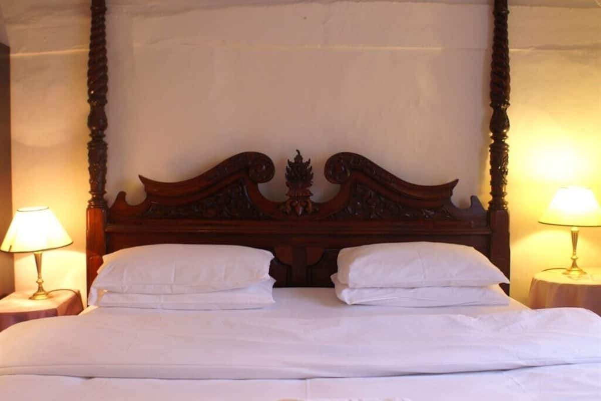 A double bed with a wooden headboard, two bedside lamps, and a neatly made bed with white linens.