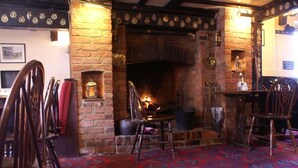 A traditional pub interior with a brick fireplace, wooden chairs, and a patterned carpet. - The Saracens Head (Amersham)