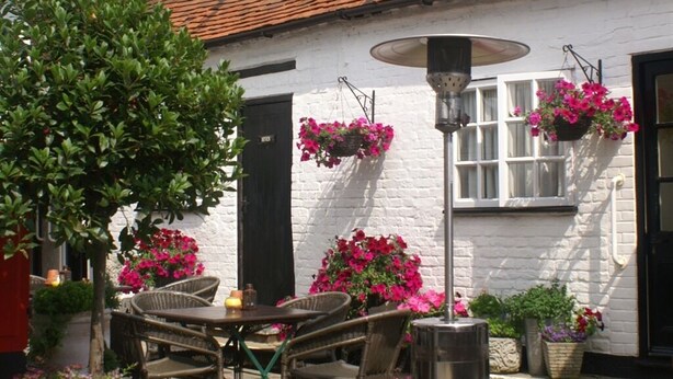 An outdoor seating area with wicker chairs and a table, surrounded by potted plants and hanging flower baskets. - The Saracens Head (Amersham)