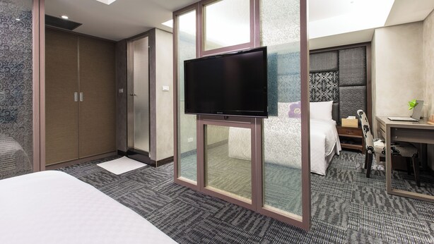 A hotel room with a large bed, a flat-screen TV mounted on a glass partition, a desk with a laptop, and a small seating area. - Han She Hotel (Taipei)