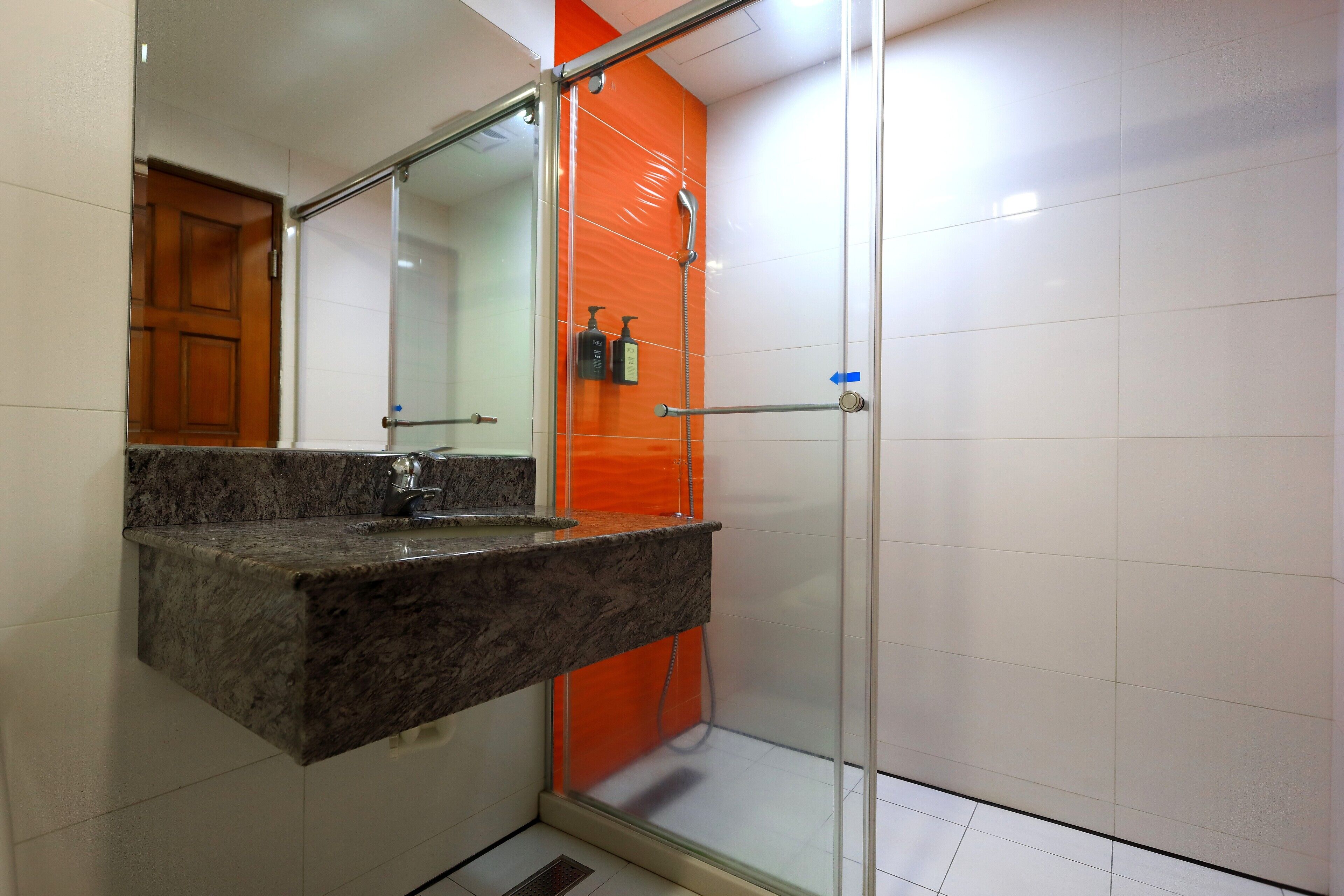 Une salle de bain avec un lavabo sur un plan de travail en granit, une douche à parois de verre et une porte en bois.