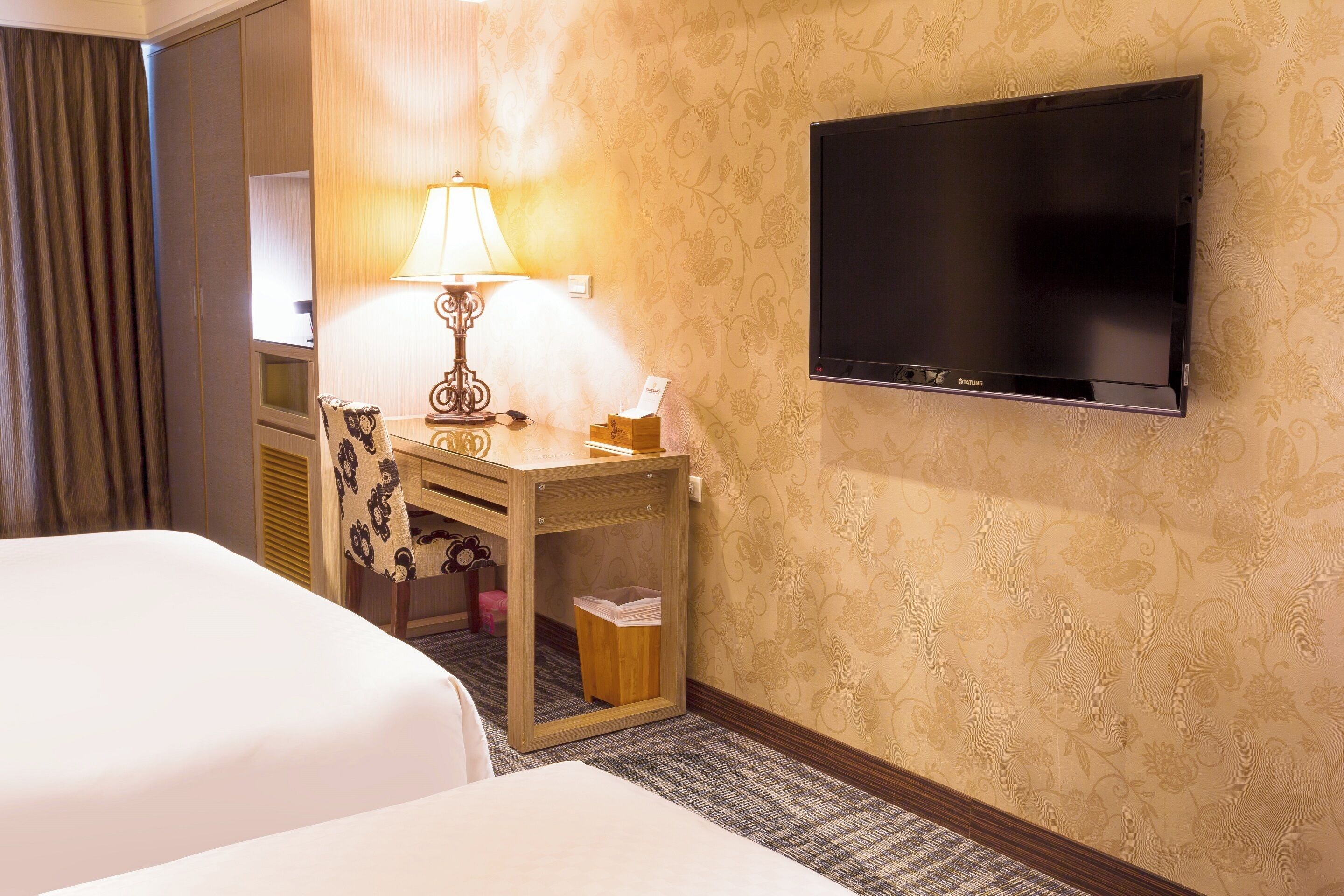 A hotel room with two beds, a desk with a lamp, a television, and a waste bin.