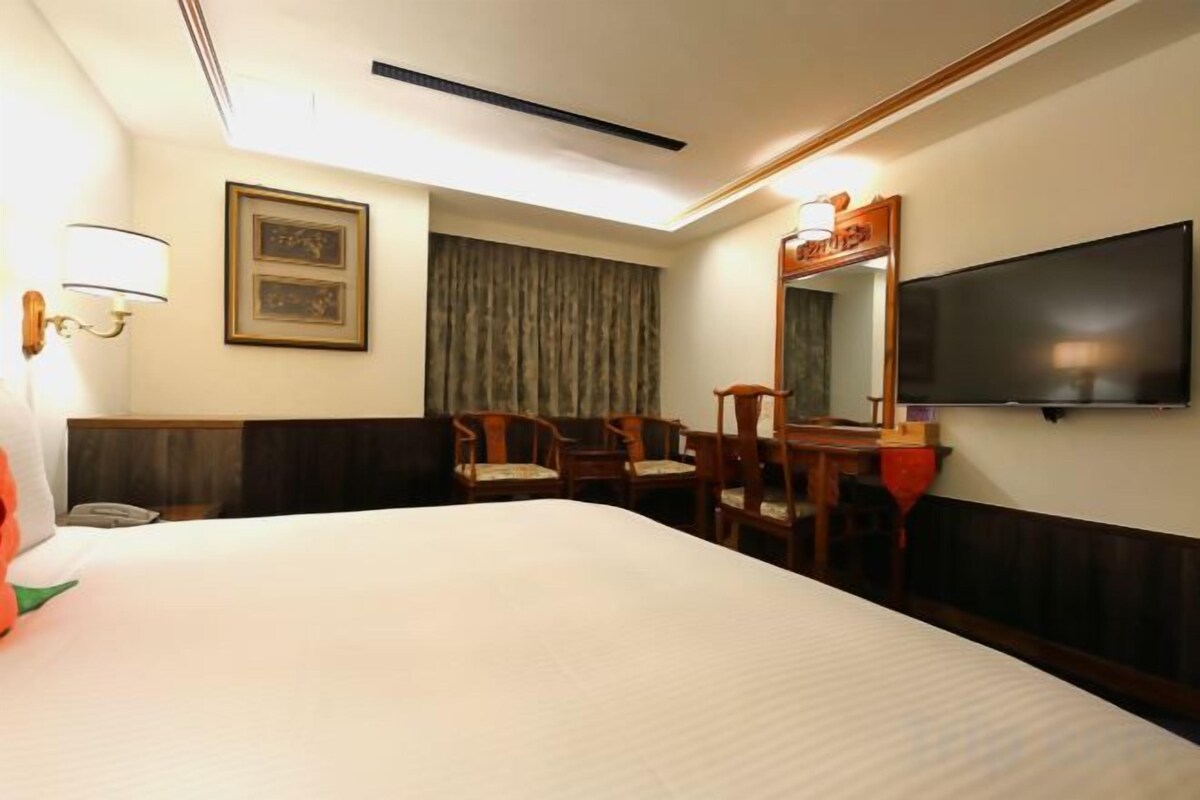 A hotel room with a large bed, a desk with chairs, a television, and a telephone.
