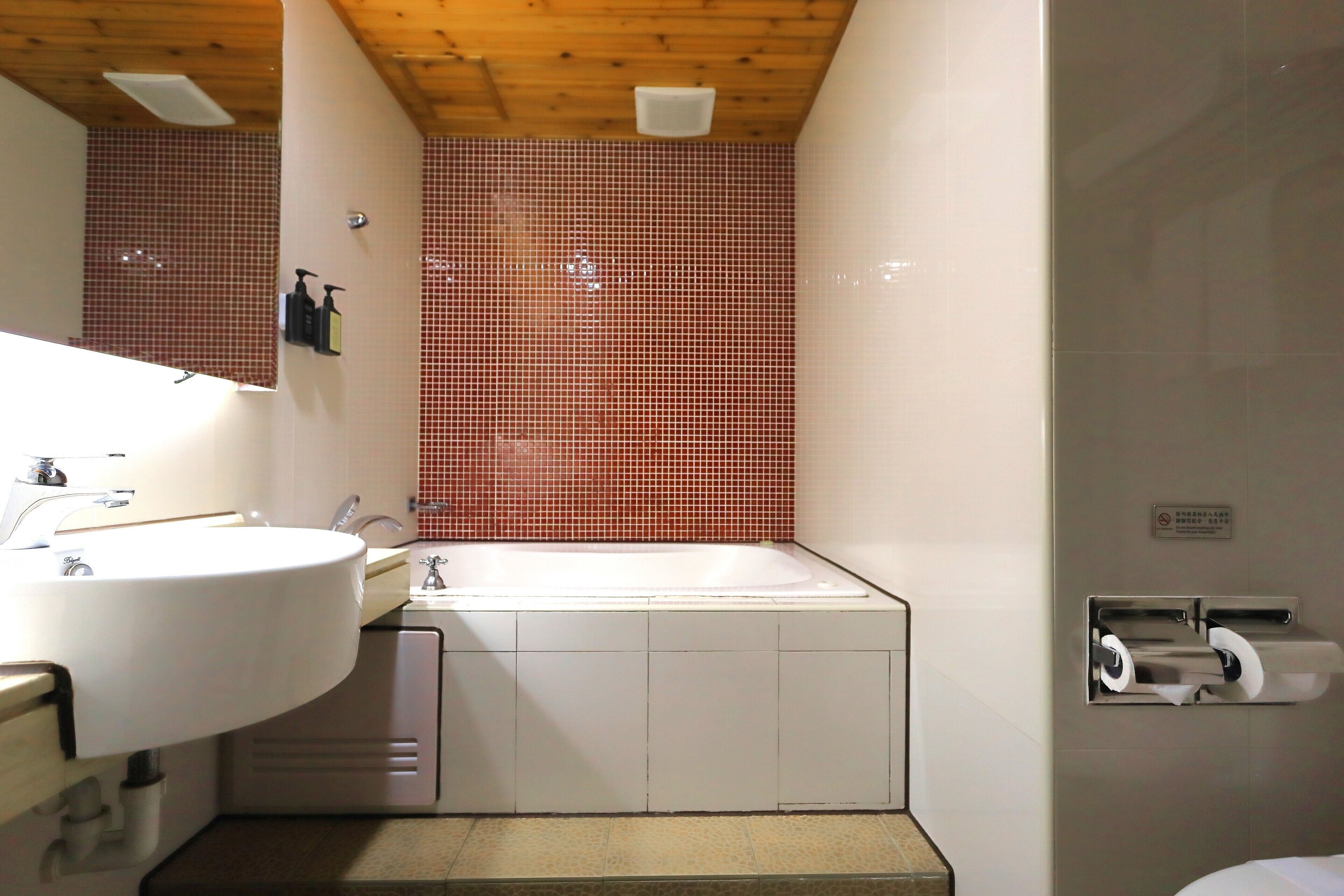 A bathroom with a white sink, a bathtub, and a toilet paper dispenser.