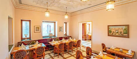 A dining area with multiple tables and chairs, a patterned ceiling, and framed artwork on the walls.