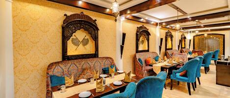 A dining area with ornate wall decorations, a chandelier, and a variety of seating arrangements.