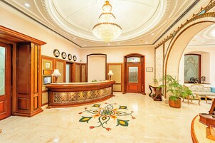 Un hall con mostrador de recepción, candelabro, diseño decorativo en el suelo y zona de estar con sofá y sillones.