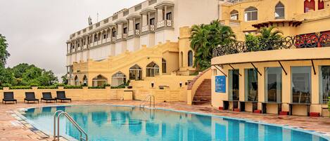 A swimming pool with a poolside area, a staircase leading to a building, and a view of the building's architecture.
