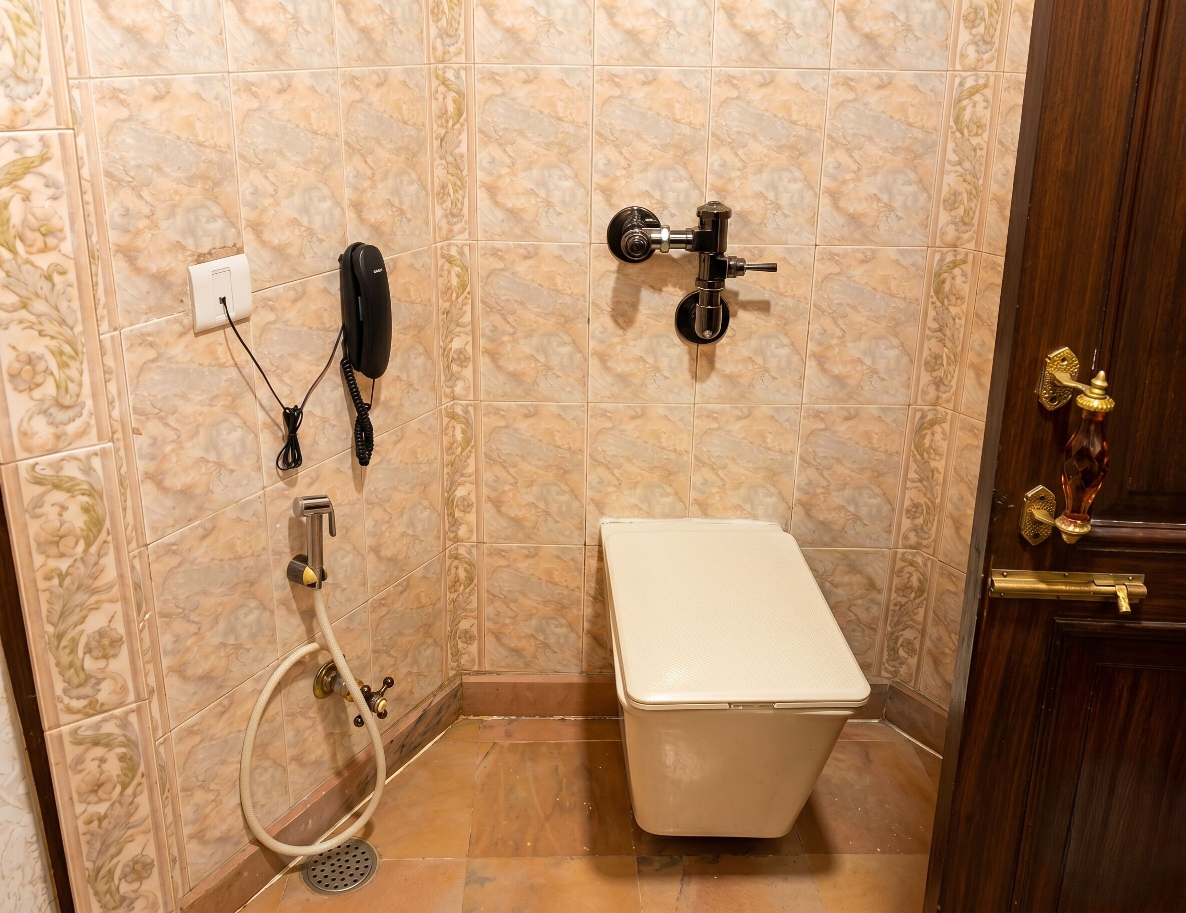 A bathroom with a toilet, a shower, a wall-mounted phone, and a door with a brass handle.