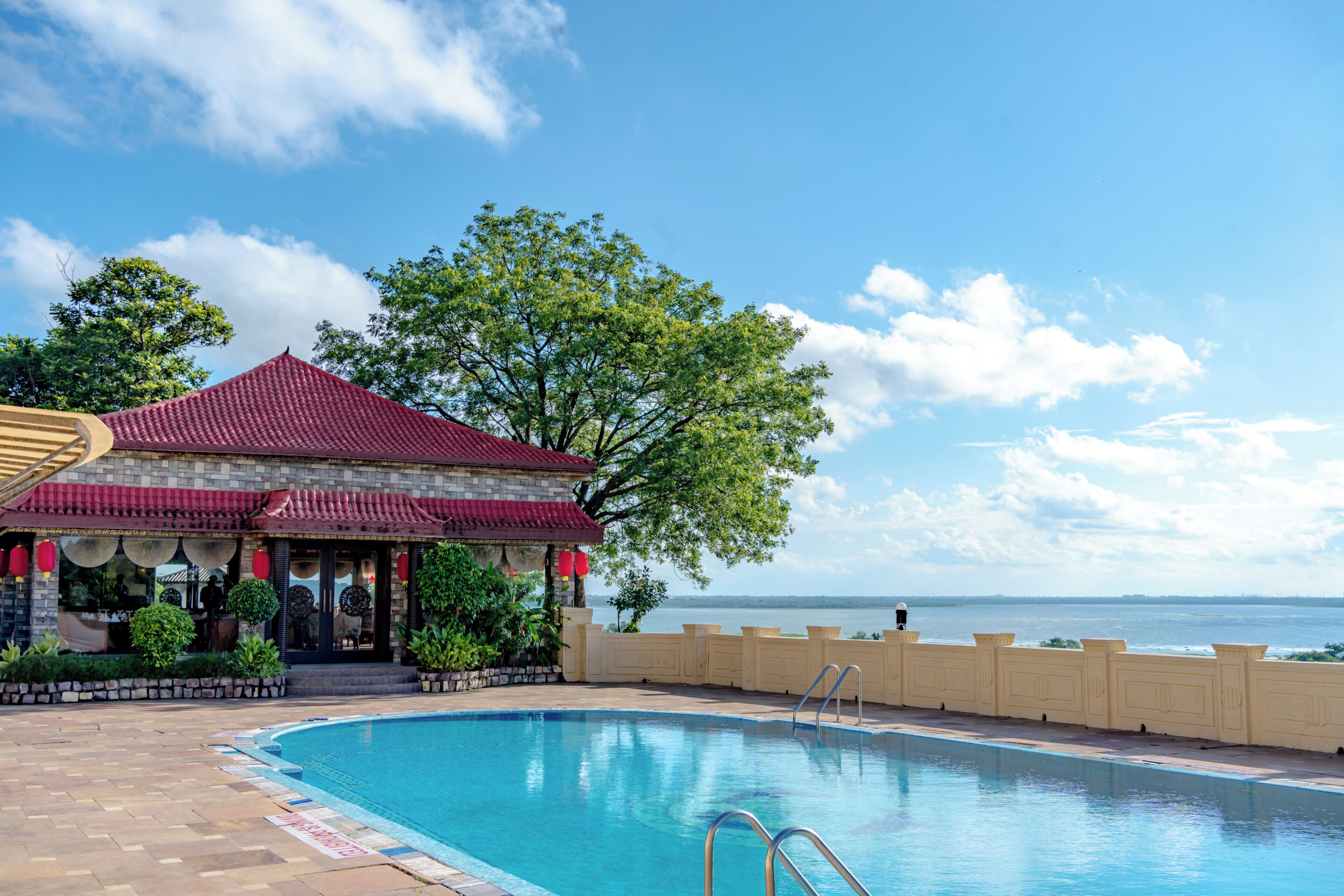 A swimming pool with a red-roofed building and a view of the water.