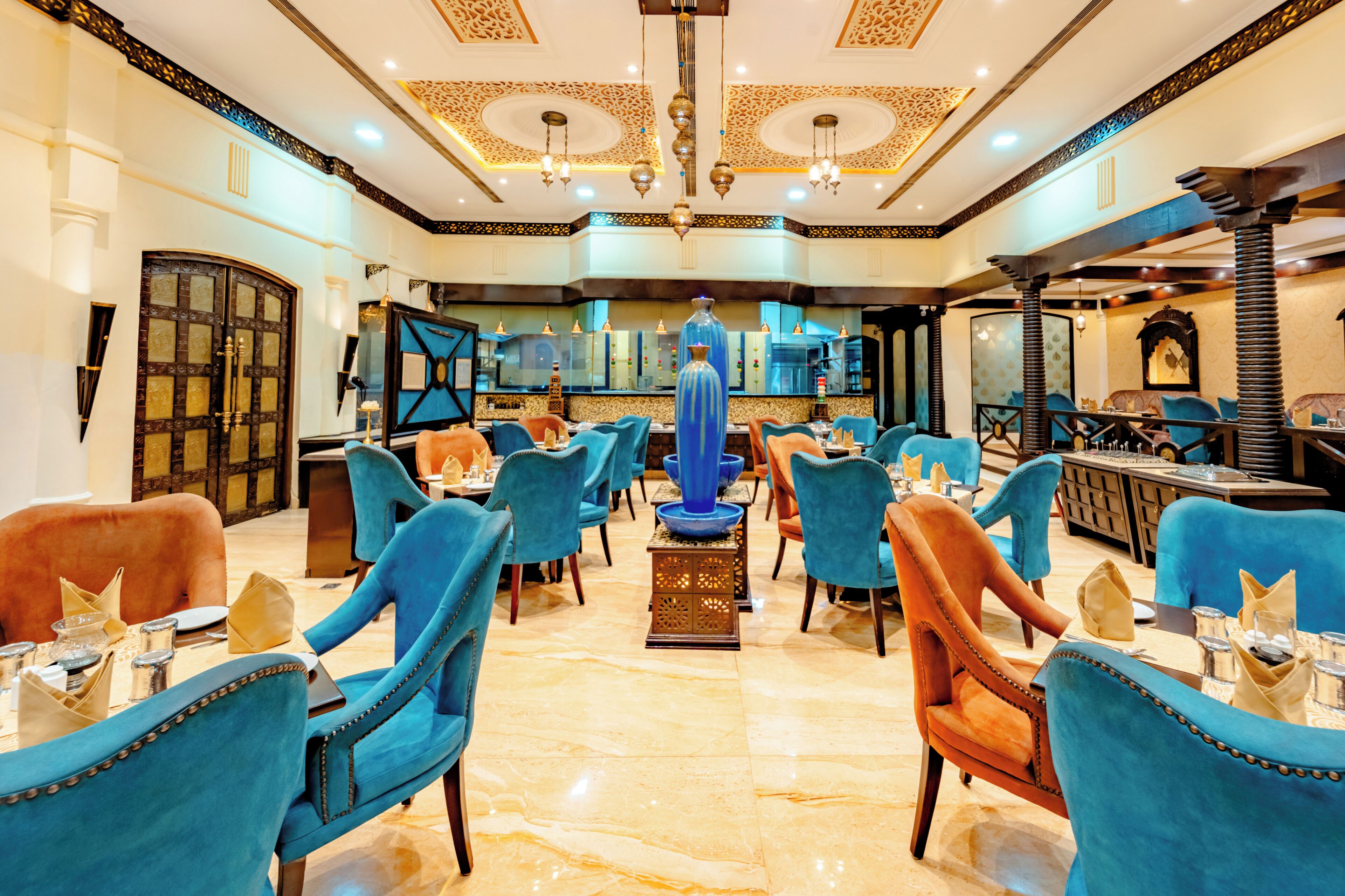 A restaurant with blue and orange chairs, a central blue vase, and a chandelier.