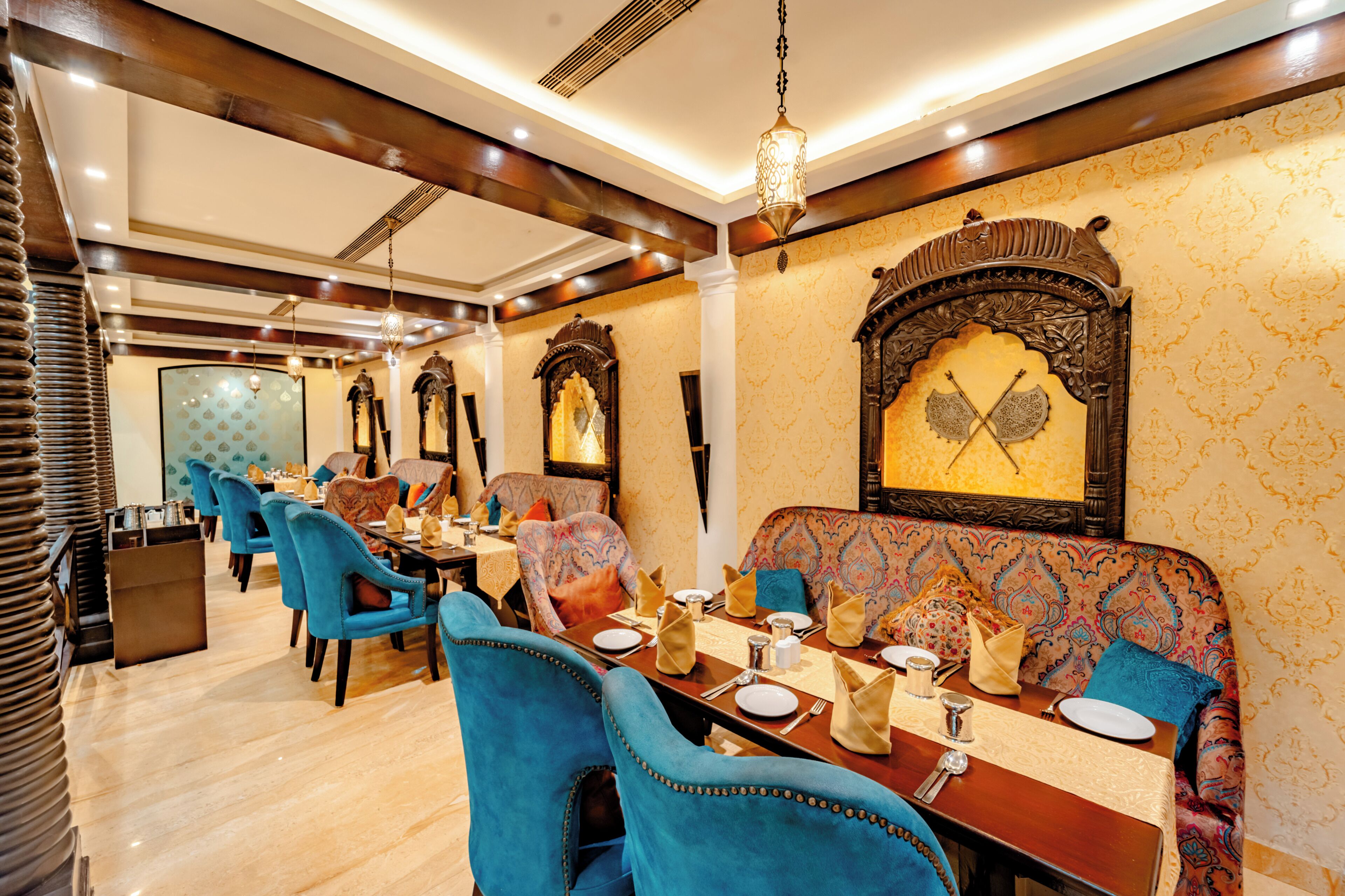 A dining area with blue chairs, a wooden table set for two, and ornate wall decorations.