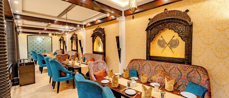 A dining area with blue chairs, a wooden table set for two, and ornate wall decorations.