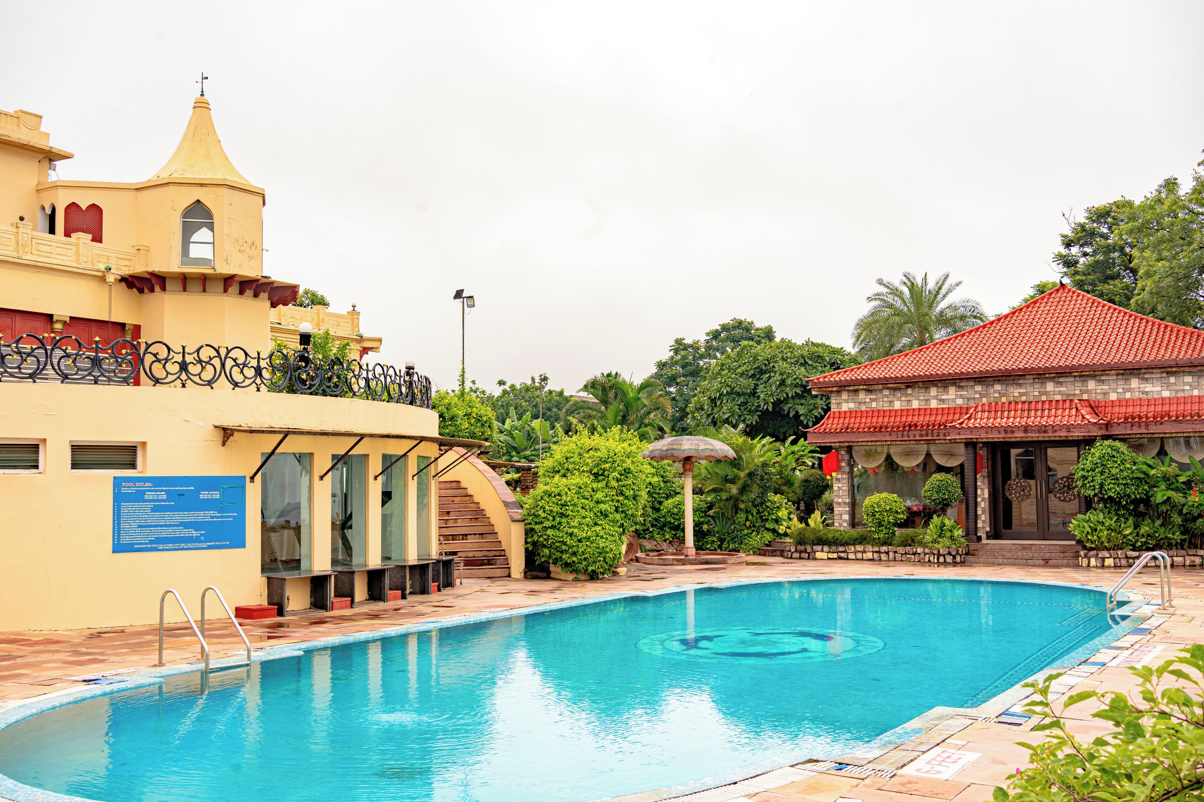 A swimming pool with a red-roofed building and a yellow building with a tower.