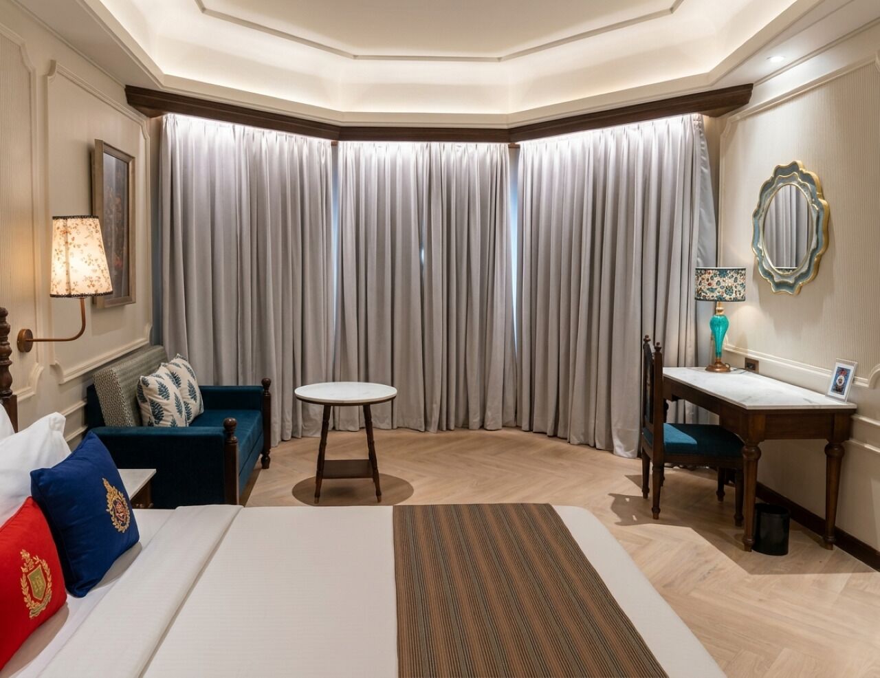 A hotel room with a bed, a desk, a chair, a small table, and a large window with curtains.