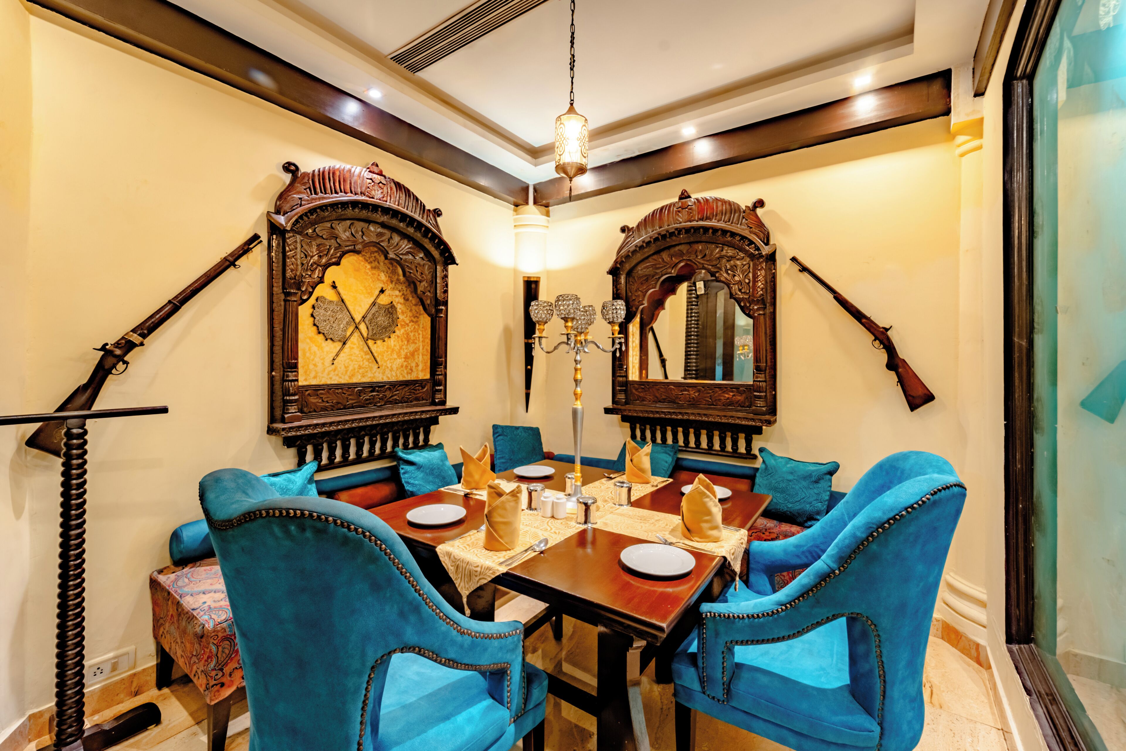 A dining area with a wooden table, blue upholstered chairs, and ornate wall mirrors.