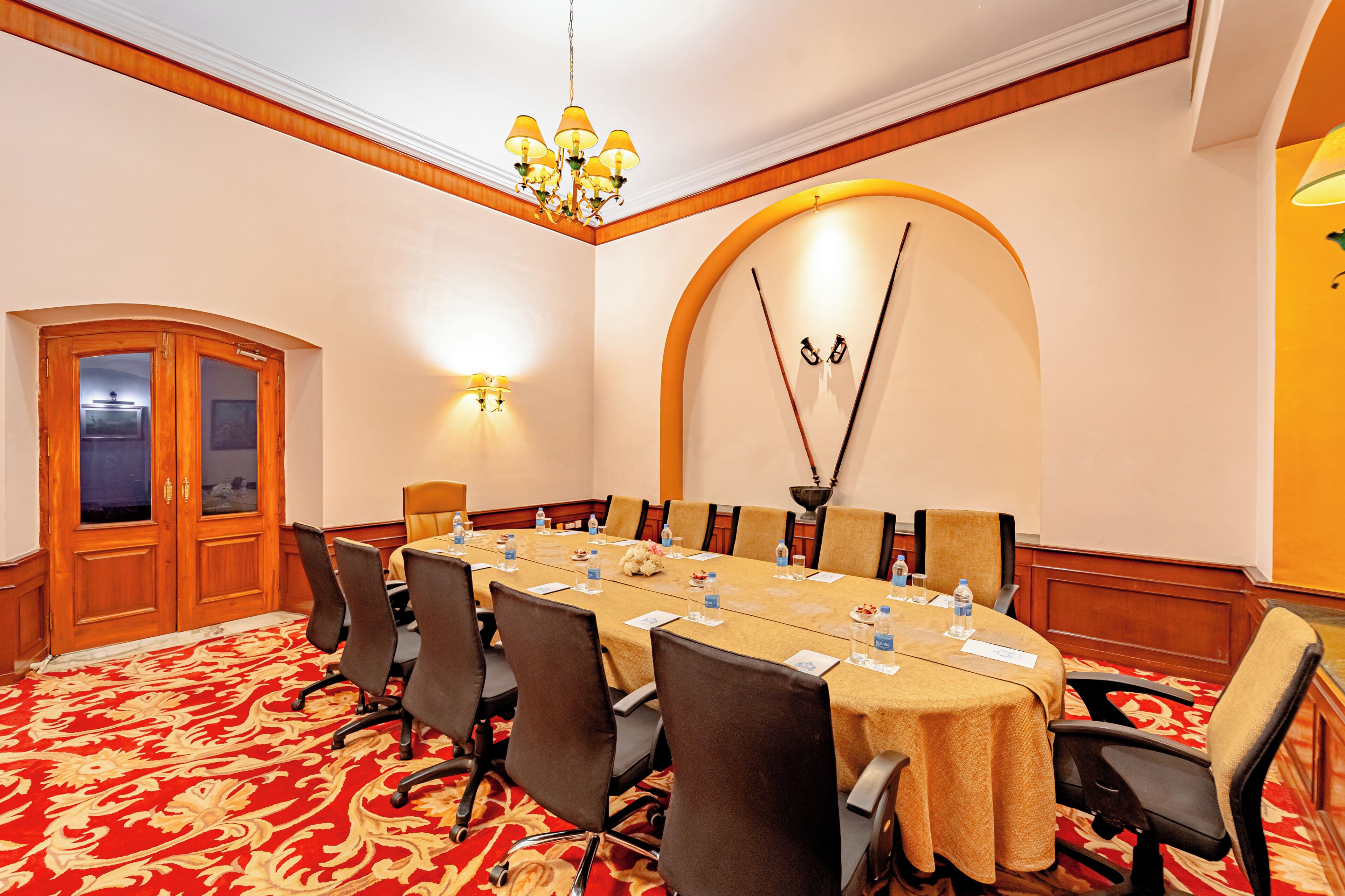 A conference room with a long table, chairs, a chandelier, and a wooden door.