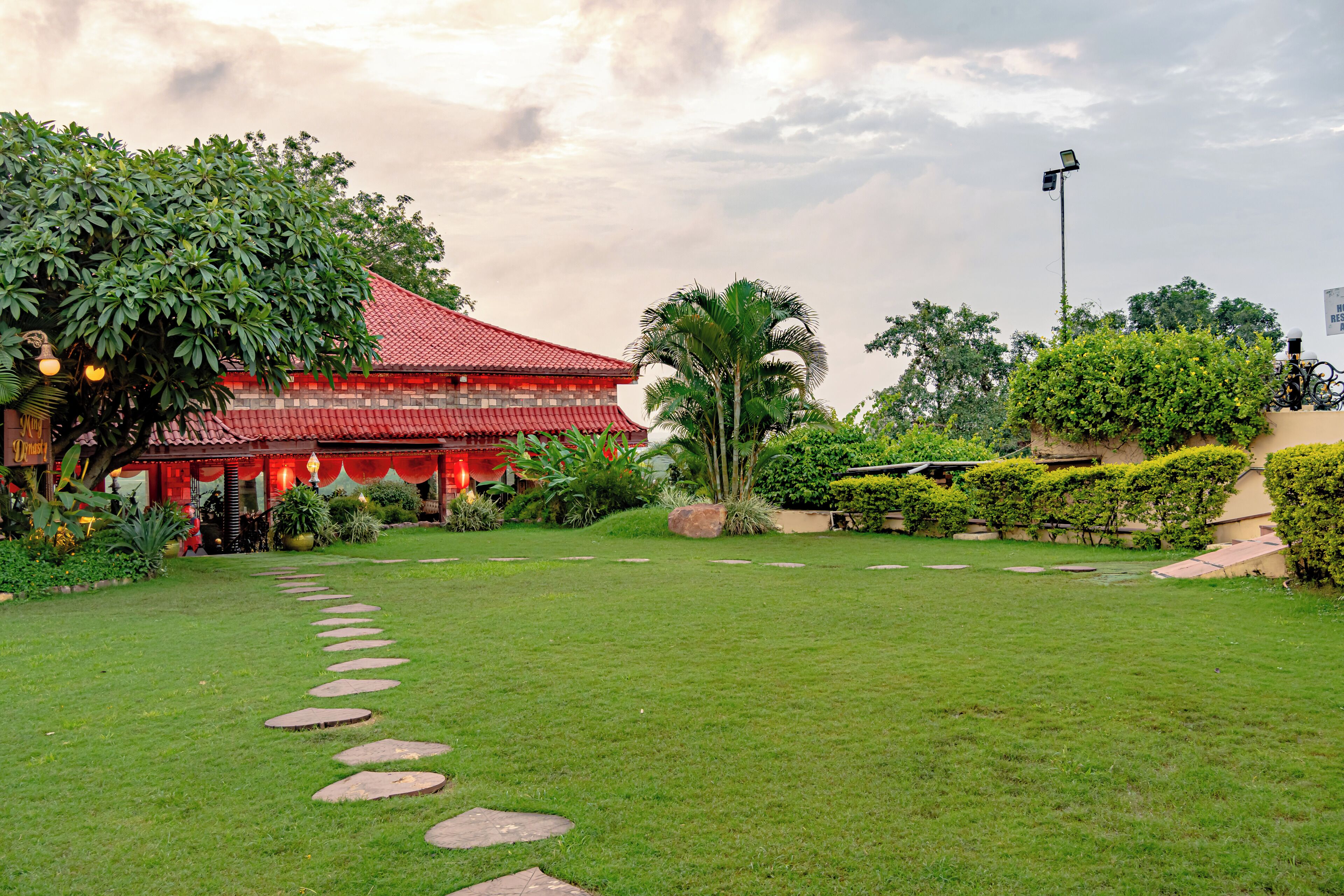 A traditional building with a red roof, surrounded by well-maintained greenery and a stone pathway.