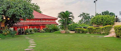 A traditional building with a red roof, surrounded by well-maintained greenery and a stone pathway.