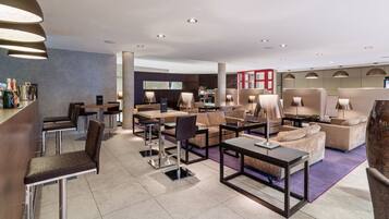 A modern hotel lobby with a bar area, seating arrangements, and a visible reception desk.